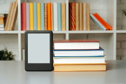 E-book reader on table against book shelves