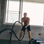 Intense muscular man training with battle rope in the fitness