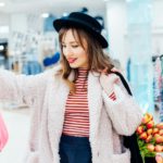 Young fashion woman customer holding magenta color dress in store. Buying clothes